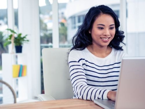 woman with dark hair and a nice smile wearing a horizontal striped shirt sitting in an office on her laptop