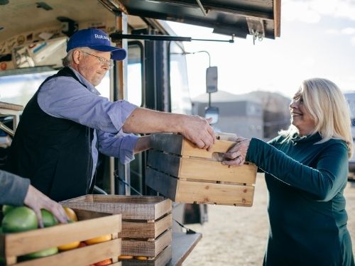 man handing box of produce to a woman at a farm stand